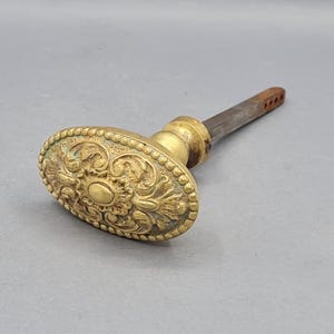 Może przedstawiać: Biały ceramiczny kubek z czarnym uchwytem i napisem "But First, Coffee" pogrubioną czcionką. Kubek stoi na drewnianej powierzchni. Kubek ma 10 cm wysokości.