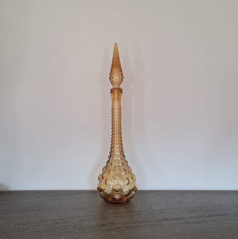 Pode incluir: Uma garrafa de vidro &acirc;mbar alta com uma superf&iacute;cie texturizada com forma de bolhas. A garrafa tem uma parte superior pontiaguda e uma base arredondada.