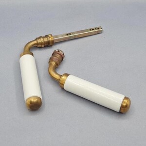 Peut inclure: Deux poignées de porte vintage avec des poignées en céramique blanche et des accents en laiton. Une poignée est détachée, montrant la pièce de montage en métal. L'autre poignée est attachée. Les poignées sont posées sur un fond gris.