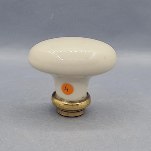 Puede incluir: Pomo de armario ovalado color crema con base de latón. El pomo tiene un acabado brillante y una pequeña pegatina naranja con el número 4. Una pieza de ferretería clásica para la restauración de muebles o nuevas construcciones.