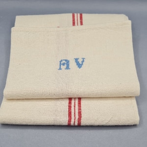 Può includere: Due asciugamani da cucina in lino bianco con strisce rosse e iniziali ricamate in blu "AV".