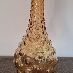Pode incluir: Um vaso alto de vidro &acirc;mbar com uma superf&iacute;cie texturizada em forma de bolhas. O vaso tem um pesco&ccedil;o estreito e uma base larga e arredondada.