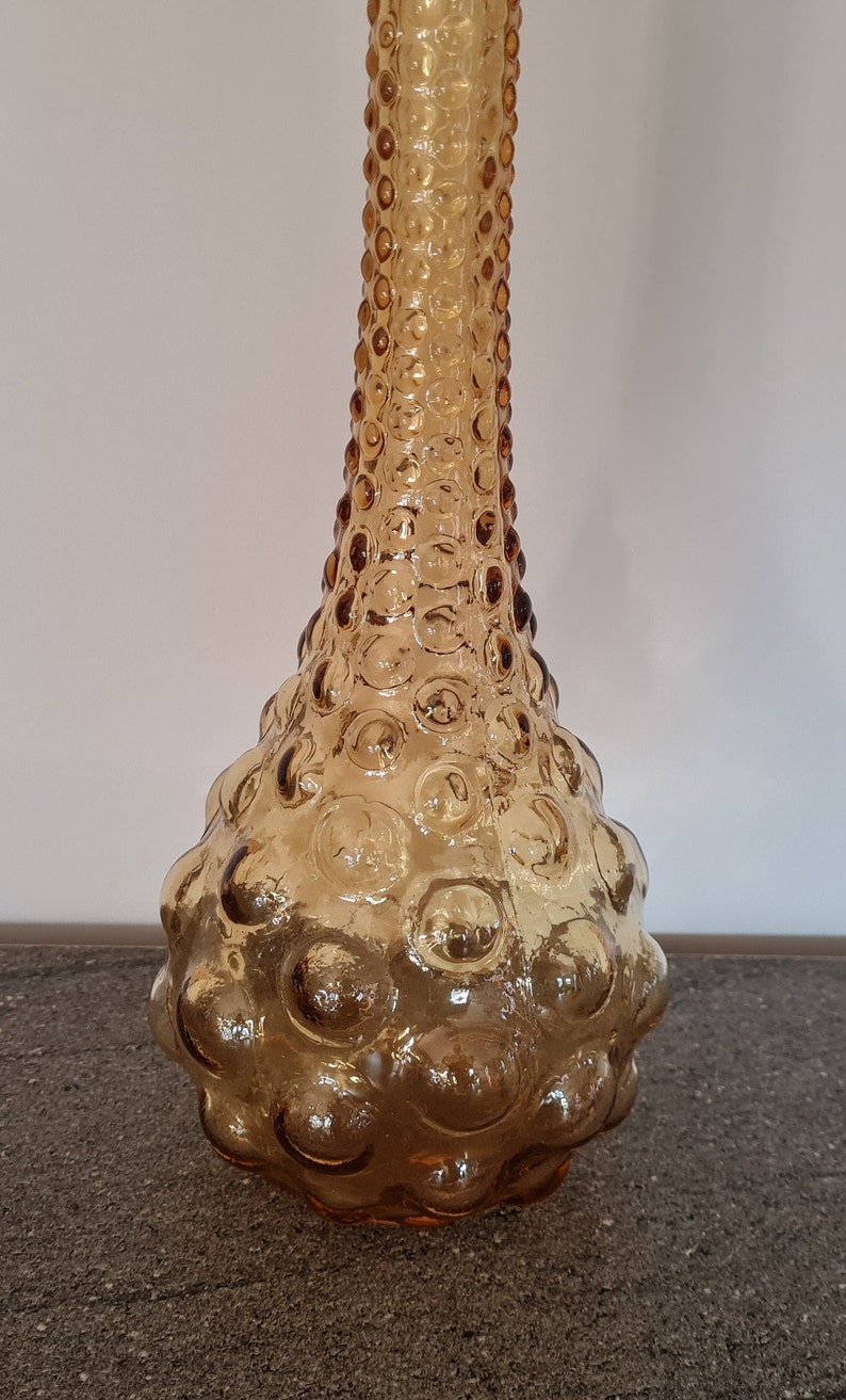 Pode incluir: Um vaso alto de vidro &acirc;mbar com uma superf&iacute;cie texturizada em forma de bolhas. O vaso tem um pesco&ccedil;o estreito e uma base larga e arredondada.