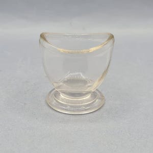 May include: A clear glass contact lens case with a rounded base and a curved top.