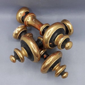 Pode incluir: Três remates decorativos pintados de preto e dourado. Os remates são de madeira e têm uma parte superior arredondada e uma base canelada.