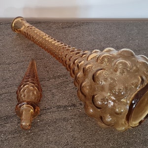 Pode incluir: Um conjunto de duas garrafas de vidro &acirc;mbar com um design texturizado em forma de bolhas. A garrafa maior est&aacute; deitada de lado, enquanto a garrafa menor est&aacute; em p&eacute;.