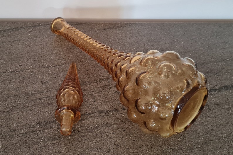 Pode incluir: Um conjunto de duas garrafas de vidro &acirc;mbar com um design texturizado em forma de bolhas. A garrafa maior est&aacute; deitada de lado, enquanto a garrafa menor est&aacute; em p&eacute;.