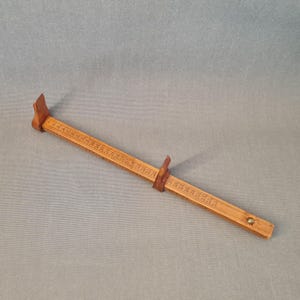 May include: A wooden measuring tool with a sliding ruler and two adjustable ends. The ruler is marked with numbers and has a brass knob at the end.