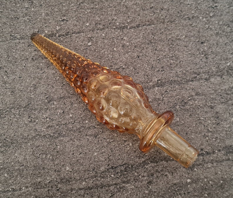 Pode incluir: Um rolha de garrafa de vidro castanho com um design texturizado e bulboso. A rolha tem uma parte superior de vidro transparente e uma base de vidro castanho.