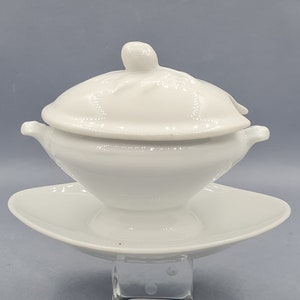 Peut inclure: Saucière en porcelaine blanche avec un couvercle et une soucoupe assortie. La saucière a un corps arrondi et une petite poignée de chaque côté. Le couvercle a un bouton sur le dessus.