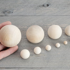 May include: A set of ten wooden balls in various sizes, ranging from small to large. The balls are all natural wood color and are arranged in a line from largest to smallest.