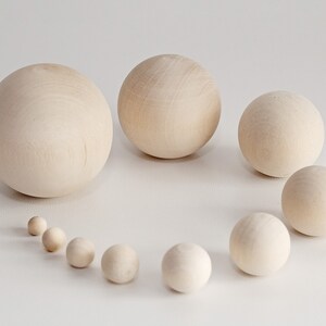 May include: A set of ten wooden balls of varying sizes, arranged in a semi-circle on a white surface. The balls are all natural wood color and smooth.