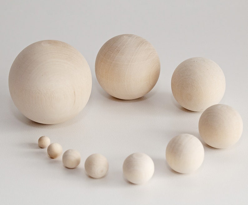 May include: A set of ten wooden balls of varying sizes, arranged in a semi-circle on a white surface. The balls are all natural wood color and smooth.