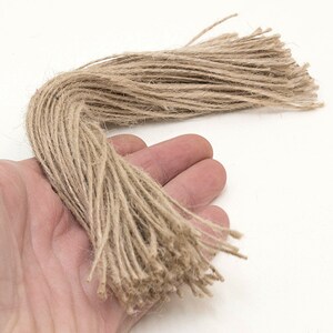 Może przedstawiać: W ręku znajduje się wiązka naturalnego brązowego sznurka, rodzaju sznurka wykonanego z wł&oacute;kien jutowych. Sznurek ma około 30 cm długości i jest luźno związany.
