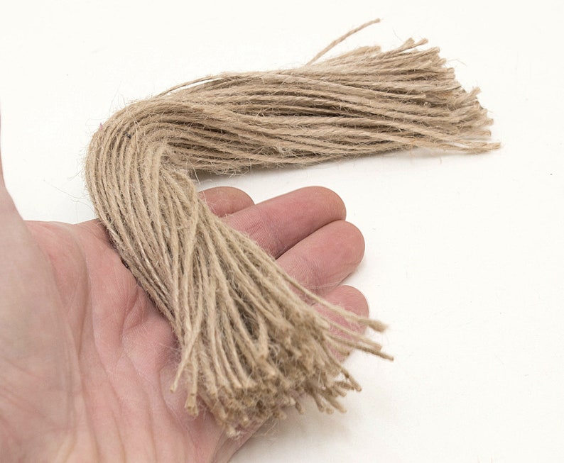 Może przedstawiać: W ręku znajduje się wiązka naturalnego brązowego sznurka, rodzaju sznurka wykonanego z wł&oacute;kien jutowych. Sznurek ma około 30 cm długości i jest luźno związany.