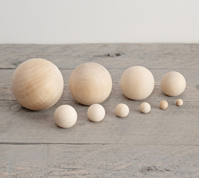 May include: A set of ten wooden balls in various sizes, ranging from small to large. The balls are all natural wood color and are arranged in a row from largest to smallest.