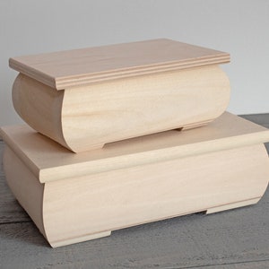 May include: Two unfinished wooden boxes, one stacked on top of the other. The boxes are rectangular with rounded sides and lids. The wood has a light, natural color.