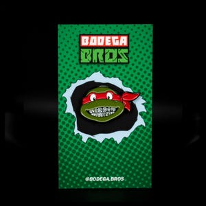 Könnte beinhalten: Ein grüner und roter Teenage Mutant Ninja Turtles-Charakter mit einem roten Bandana und Zahnspange ist auf einem grün-weißen Hintergrund mit dem Text "BODEGA BROS" und "@BODEGA.BROS" abgebildet.