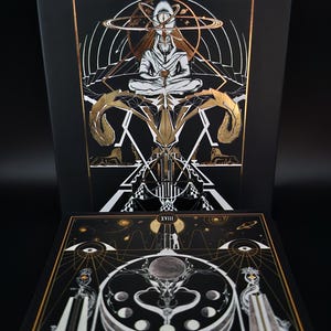 May include: Black tarot card box with gold foil accents and the name "INA AUDERIETH" at the top. The box features an illustration of a figure in meditation, surrounded by celestial elements. The bottom card displays a celestial design with the Roman numeral XVIII.
