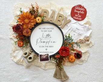 Könnte beinhalten: Ein rundes Schild in Schwarzweiß mit dem Text "We are excited to say our little pumpkin is on the way!" und "November 2024". Das Schild ist von Herbstdekorationen umgeben, darunter ein Baby-Strampler, ein Kürbis und Herbstblätter.