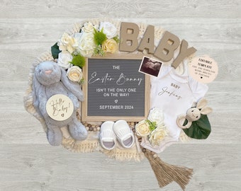 May include: A baby announcement with a letter board that reads "The Easter Bunny isn't the only one on the way! September 2024". The announcement also includes a white onesie with the text "Baby Jerfing", a gray bunny, white booties, and a wooden sign that says "Hello Baby!"