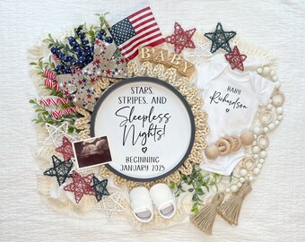 May include: A white onesie with the text "Baby Richardson" in black lettering. A wooden sign with the text "Stars, Stripes, and Sleepless Nights! Beginning January 2025" is surrounded by red, white, and blue stars, a small American flag, and a wooden block spelling "Baby".