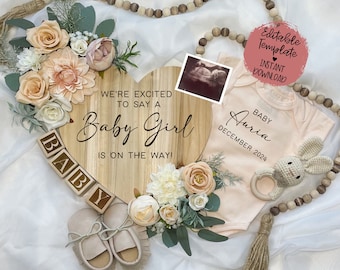 May include: A wooden heart-shaped sign with the text "We're excited to say a Baby Girl is on the way!" surrounded by peach and white flowers, a baby onesie with the text "Baby Auria December 2024", and a wooden block spelling "BABY".