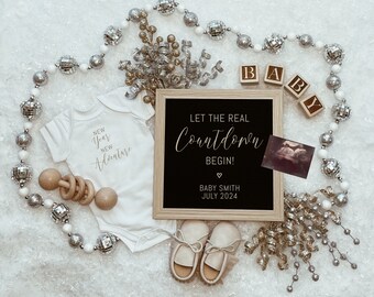 Puede incluir: Un body blanco con el texto "New Year New Adventure" en letras doradas, un sonajero de madera, un letrero de pizarra enmarcado con el texto "Let the Real Countdown Begin! Baby Smith July 2024", y una guirnalda decorativa plateada y dorada.