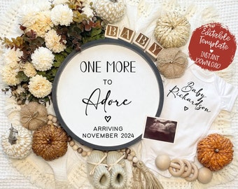 Könnte beinhalten: Ein weißes Holzschild mit dem Text "One More To Adore" und "Arriving November 2024". Das Schild ist von Herbstdekorationen umgeben, darunter kleine Kürbisse, ein Baby-Strampler und ein Holzblock, der "BABY" buchstabiert.