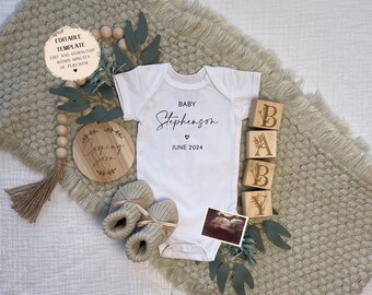 May include: A white baby onesie with the text "BABY Stephenson" and "JUNE 2024". A wooden sign with the text "Coming Soon" is in the background. There are also wooden blocks that spell out "BABY" with floral designs.