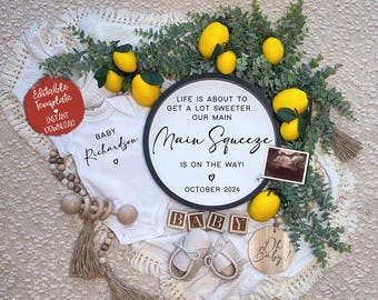 May include: A black and white round sign with the text "Life is about to get a lot sweeter... Our Main Squeeze is on the way! October 2024". The sign is surrounded by lemons and greenery. There is a white onesie with the text "Baby Richardson" and a small ultrasound image.