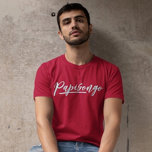 May include: A person wearing a red t-shirt with the text "Papisongo" in white lettering. The person is holding a black tote bag with the text "Sabroso Streetwear" in pink, orange, and yellow lettering. The bag also has the text "Streetwear. With Flavor." in white lettering.