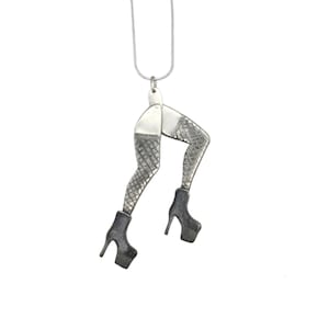Puede incluir: Un collar de plata con un colgante en forma de piernas que llevan medias de rejilla y tacones altos.