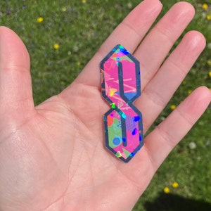 May include: A pink and black sticker with a geometric pattern in the shape of the letter "S".