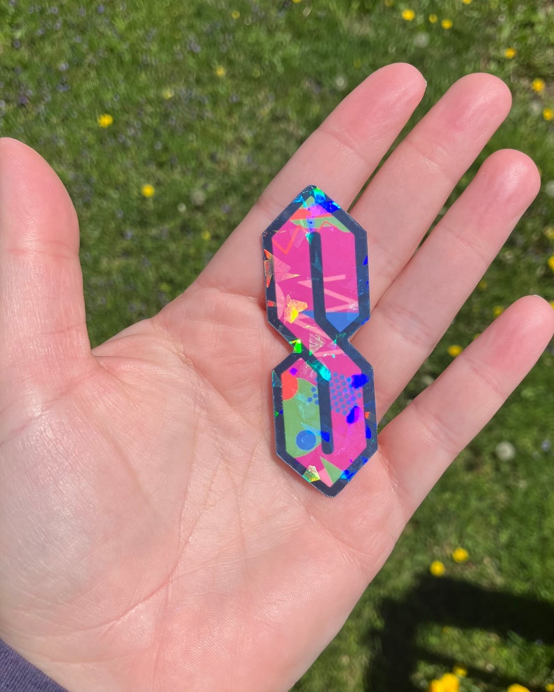 May include: A pink and black sticker with a geometric pattern in the shape of the letter "S".