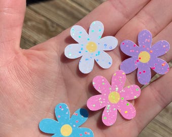 May include: Four glitter flower stickers in different colors: white, pink, purple, and blue. Each flower has a yellow center.