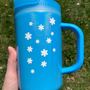 May include: A blue stainless steel tumbler with a white floral design and a lid with a straw. The tumbler has a handle and a glittery finish.