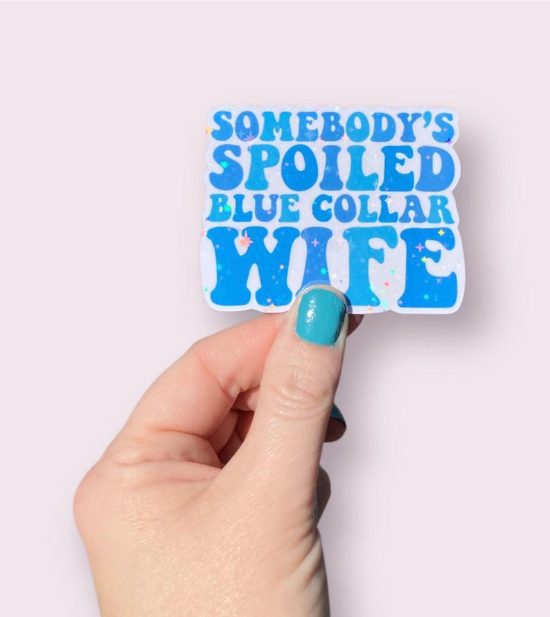 May include: A blue and white sticker with the text "Somebody's Spoiled Blue Collar Wife" in a retro font. The sticker has a glittery finish.