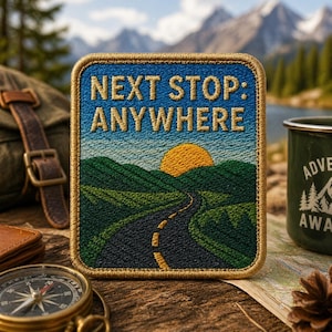 Puede incluir: Parche bordado con el texto "NEXT STOP: ANYWHERE" sobre una escena de paisaje de una carretera que serpentea hacia un sol poniente. El parche tiene un cielo azul, colinas verdes y un borde dorado. Una brújula, una taza y un mapa están en el fondo.