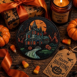 May include: A circular embroidered patch featuring a haunted house scene with a large orange moon, glowing windows, and two jack-o'-lanterns on the lawn. The detailed stitching depicts a dark, atmospheric landscape with a winding path leading to the house.