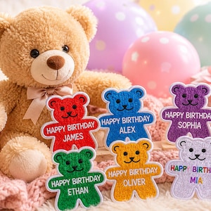 May include: A soft brown teddy bear with a bow, alongside colourful balloons and birthday patches. The patches are bear-shaped and feature the words "Happy Birthday" and names such as "James" and "Alex".