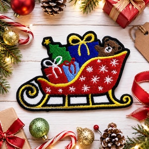 May include: A festive embroidered patch featuring a red sleigh decorated with white snowflakes, carrying a green Christmas tree, a blue gift box with a yellow bow, a red gift box with a white bow, and a small brown teddy bear inside.