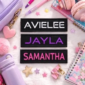May include: Three rectangular black embroidered patches featuring the names AVIELEE in white, JAYLA in purple, and SAMANTHA in pink. Each patch has a stitched border and is arranged vertically on a white surface surrounded by various school supplies.