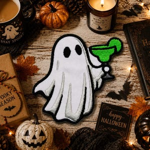 May include: An embroidered patch featuring a white ghost with black eyes holding a green margarita glass. The ghost has a black border and is depicted with a draped, flowing sheet design. The patch is a flat, fabric-based item with detailed stitching.