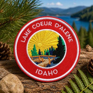 Può includere: Toppa rotonda ricamata con la scritta "Lake Coeur d'Alene Idaho". La toppa ha un bordo rosso con cuciture bianche. Il centro raffigura un sole giallo, alberi e un lago. Articolo da souvenir.