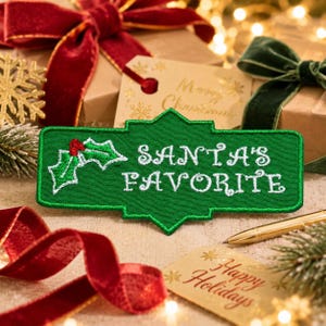 May include: A rectangular green embroidered patch with a decorative border featuring the white stitched text SANTA'S FAVORITE and a small holly leaf graphic with red berries on the left side, presented as a festive holiday accessory.