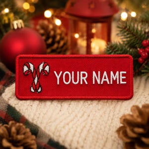 May include: A red rectangular patch with the text "YOUR NAME" in white. The patch features two crossed candy canes with red and white stripes. The patch is set against a festive background with Christmas decorations and foliage.