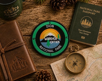 May include: A circular embroidered patch featuring a mountain landscape, the text Zion National Park, and the words Wander Often. The patch is surrounded by a green mug, a brown leather journal, a National Park Passport, a compass, and pinecones.