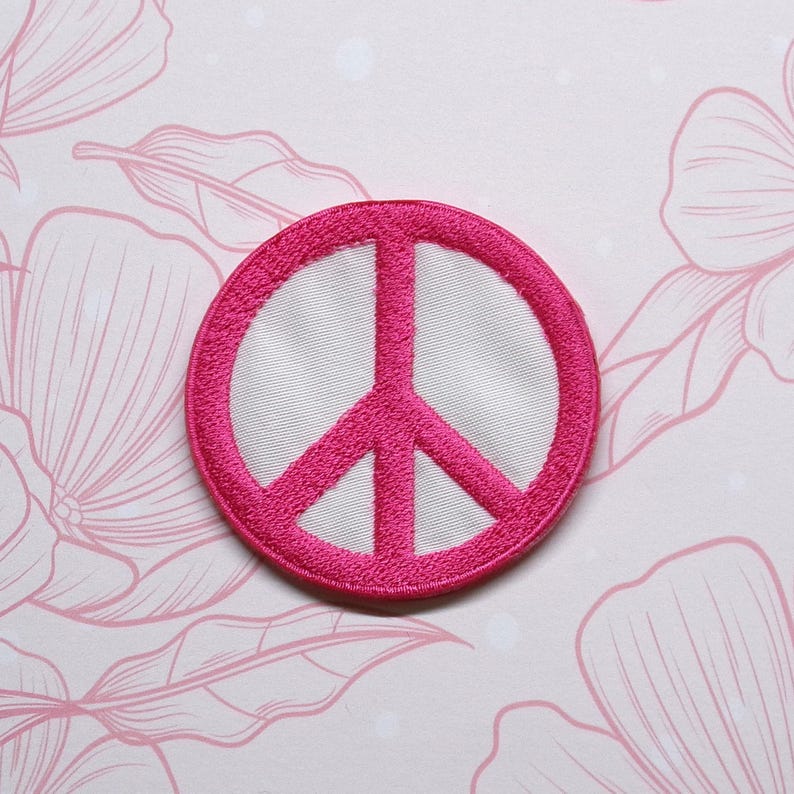 May include: A pink peace sign embroidered patch. The patch is circular and has a white background.