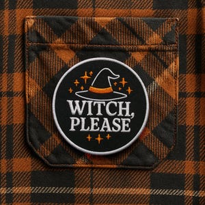 May include: Close-up of a black and orange plaid fabric with a pocket. A circular patch on the pocket reads "WITCH, PLEASE" with a witch hat and stars. The patch is white with black and orange details. Halloween themed.